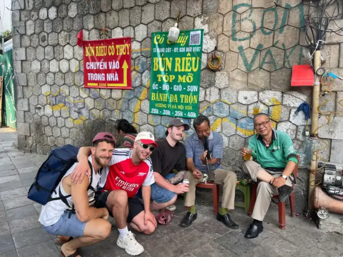 Travelers joining a Hanoi private tour sitting with locals and enjoying street food in the Old Quarter