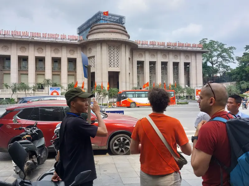 Hanoi private tour with local guide explaining Vietnamese history to travelers in front of the State Bank of Vietnam